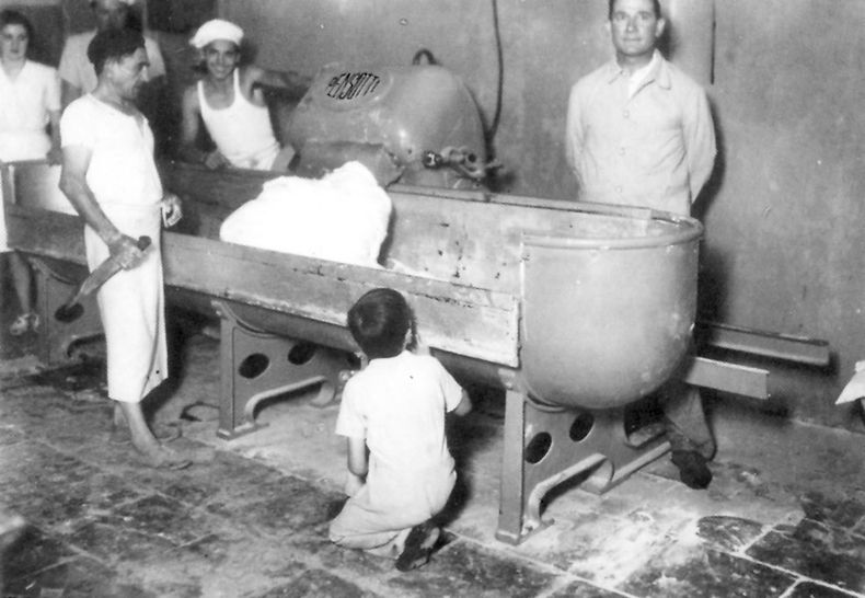 Don Mateo Marconcini (der.) junto a la máquina amasadora, supervisa el trabajo de sus empleados en la panadería “El Molino”. La foto fue tomada en el año 1946, año de su fundación.&nbsp;
