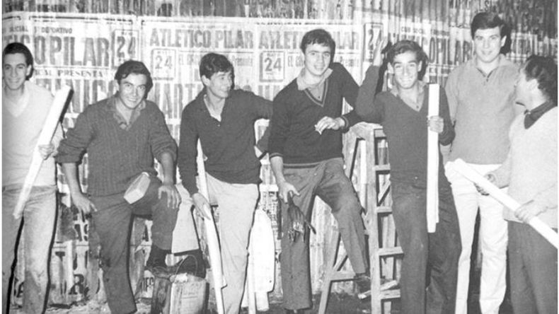 Los socios adolescentes del Club Atlético Pilar hacen una pegatina de afiches en las paredes del centro, anunciando los bailes que se harían en la institución ese fin de semana de 1967..