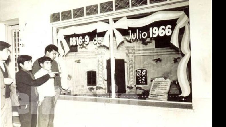 Julio de 1966. Moderna mueblería Rivadavia, de Domenech y Gabrielle, en Rivadavia y Gamboa. Era costumbre del comercio decorar la vidriera para conmemorar las fechas patrias. Vemos a los aprendices de carpintería Pereyra, los hermanos Acobo y Ocampo, satisfechos con su obra artesanal..