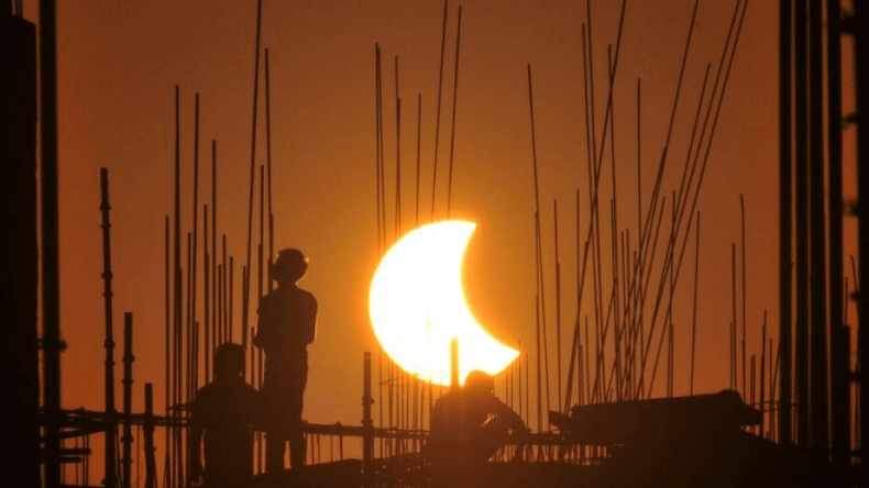 Los trabajadores trabajan en un sitio de construcción mientras la luna oscurece parcialmente el sol durante un eclipse solar parcial visible desde Gurgaon el 25 de octubre de 2022. | Crédito: Vinay GUPTA / AFP .