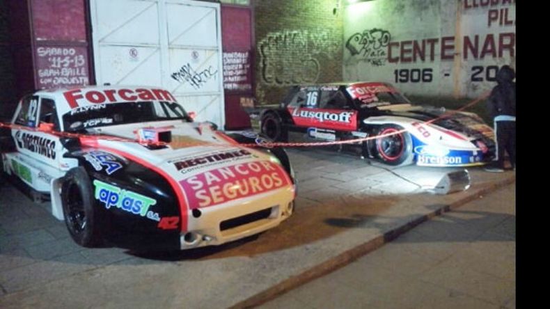 Una postal pocas veces vista: dos autos de Turismo Carretera en la vereda del Club Atlético, y en marcha..