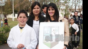 César junto a una docente y la directora de su escuela, quien sostiene el nuevo escudo de la localidad..